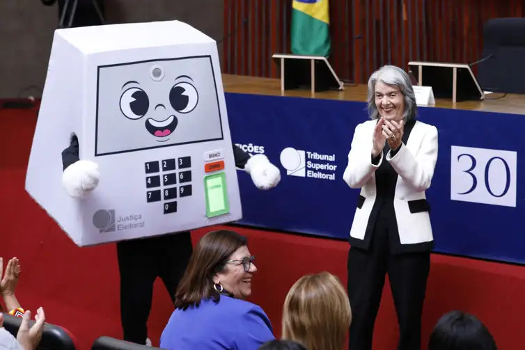 Brasília (DF), 01/05/2026 - Mascote do TSE e a ministra Cármen Lúcia durante cerimônia de comemoração aos 30 anos da Urna Eletrônica. Foto: Alejandro Zambrana/Secom/TSE